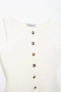 Detailed view of white ribbed knit vest featuring large textured gold buttons and round neck