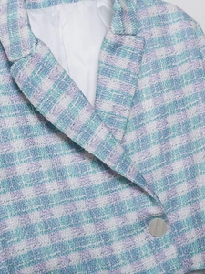 Detailed close-up of blue-purple tweed blazer texture with a silver metal button
