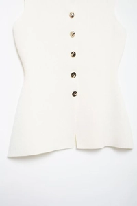 Close-up of white ribbed knit vest featuring metallic gold buttons and irregular hemline