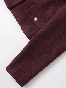 Detail of burgundy tweed jacket featuring a textured pocket and a gold rope button