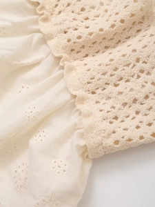 Detail of cream crochet knit bodice and floral eyelet embroidery with ruffle seams