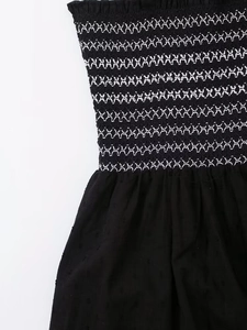 Detail view of black dress featuring smocked elastic bodice with white geometric embroidery
