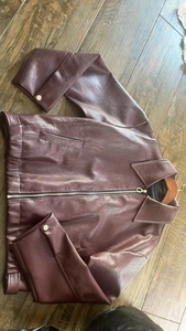 Flat lay of burgundy leather jacket with metal zippers on dark wood background
