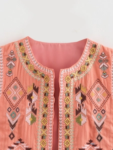 Detailed close-up of geometric embroidery and natural texture on a coral cotton vest