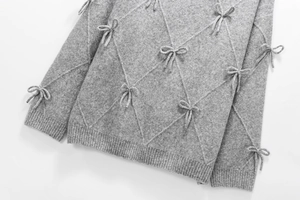Detailed view of grey knit sweater featuring 3D bow accents and classic diamond patterns