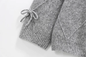 Detailed view of grey knit sweater with diamond pattern and bow tie on the ribbed cuff