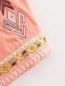 Detailed close-up of bohemian geometric embroidery on orange-pink cotton linen vest