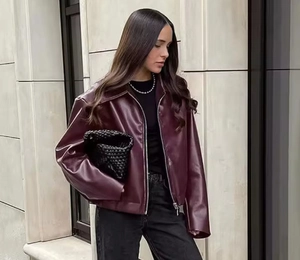 Detail shot of a burgundy faux leather jacket featuring classic lapel and metallic zippers