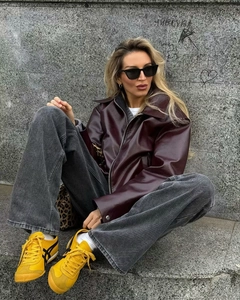 Detail of burgundy glossy leather jacket paired with washed wide-leg grey denim jeans
