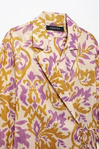 Close-up of baroque floral pattern on silk-textured jacket with gold and purple tones