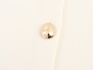 Dettaglio di un gilet in maglia bianco con bottone d'oro lucido e trama fine