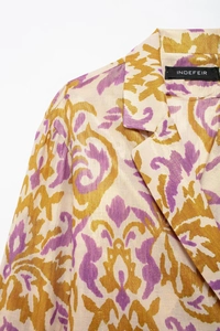 Detail of metallic jacquard fabric with purple and yellow swirl patterns on blazer