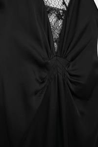 Détail de la robe noire à col en V avec dentelle florale délicate et tissu plissé soyeux