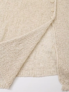 Detail of warm beige hollow knit cardigan featuring side slits and pearly buttons