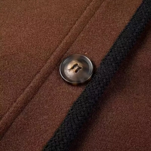 Close-up of wool jacket with brown button and black braided trim detail