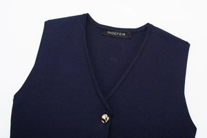 Close-up of navy knit vest V-neckline featuring a signature tag and polished gold button