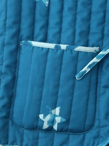 Detail der petrolfarbenen Steppweste mit Längsnähten und Sternmuster auf der Tasche