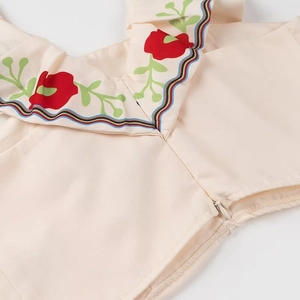 Detail of cream fabric with floral embroidery and colorful wavy trim around neckline