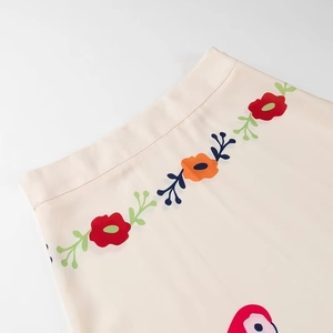 Detailed view of floral print and bird motifs on a silky beige high-waist midi skirt