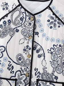 Macro detail of quilted paisley floral jacket with amber buttons and black piping finish