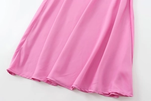 Détail macro de l'ourlet lisse et de la texture plissée sur cette robe midi en satin rose