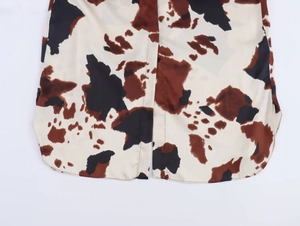 Detailed view of the cow print shirt hem featuring side slits and curved stitching
