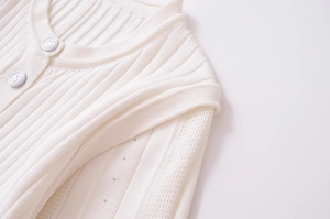 Dettaglio di cardigan in maglia a coste bianca con bottoni a S e punti traforati