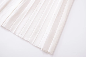 Dettaglio del tessuto a maglia plissettato bianco con occhielli decorativi sull'abito