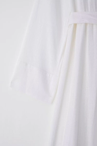 Close-up of white linen shirt dress showing waist tie and cuff stitching details