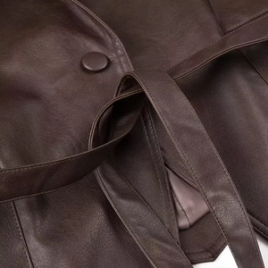 Détail d'un manteau en cuir marron foncé avec ceinture et bouton rond assorti