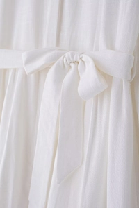 Detail shot of a white midi dress featuring a tied waist belt and textured linen fabric