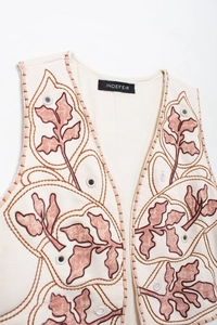 Dettaglio ricamo con specchietti decorativi su un gilet boho color crema