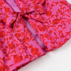 Detailed view of pink vest featuring red floral patterns and decorative front bow tie
