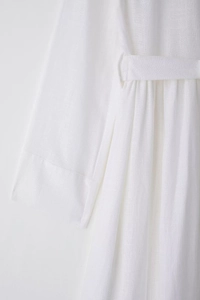 Close-up of white cotton linen midi dress showing sleeve detail and waist tie texture