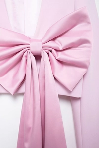 Détail du blazer en satin rose avec un grand nœud 3D et une finition lisse