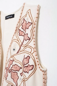 Dettaglio del gilet bianco sporco con ricamo di foglie marroni e decori a specchio