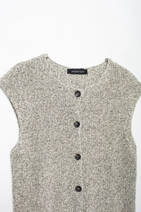 Close-up of knit vest featuring a round neck with black buttons and woven texture