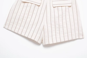 Detail view of cream cotton-linen shorts with red vertical stripes and pocket stitching