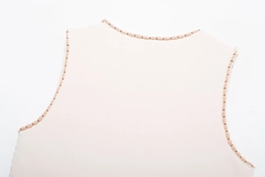 Dettaglio macro del top beige senza maniche con bordo decorativo marrone cucito a mano