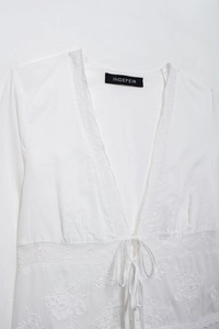 Détail du chemisier blanc avec broderie florale, bordure en dentelle et lien au col V