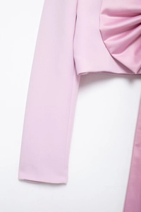 Détail d'un blazer en satin rose clair avec un grand nœud décoratif et texture raffinée