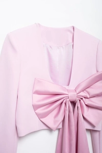 Détail du grand nœud en satin sur un blazer rose montrant la texture du tissu de qualité