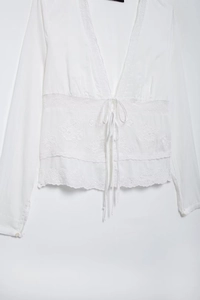Détails de broderie sur chemisier blanc avec dentelle florale et décolleté en V à nœud