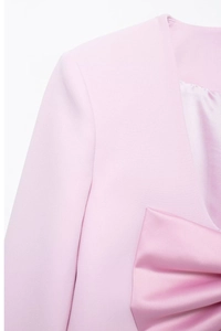 Détail d'un blazer rose clair avec un grand nœud en satin et texture tissée lisse
