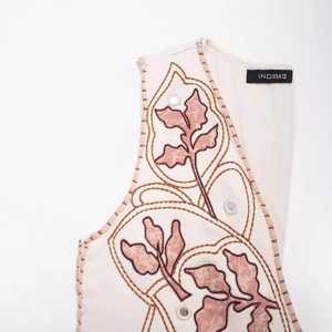 Gilet senza maniche crema con ricamo di foglie rosse e dettagli con occhielli metallici