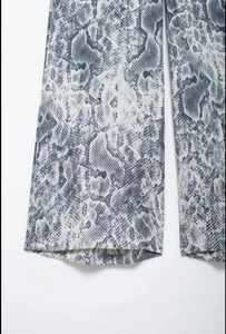 Close-up detail of light gray snakeskin print on wide-leg trousers fabric