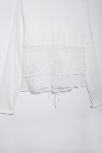 Détail d'une blouse blanche avec broderie florale et finitions en dentelle fine