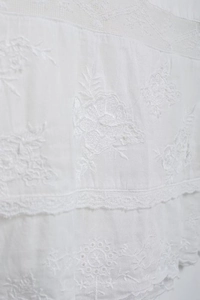 Détail rapproché du tissu brodé blanc avec motifs floraux et finitions en dentelle