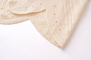 Detailed close-up of cream knit fabric with hollow pointelle patterns and scalloped edges