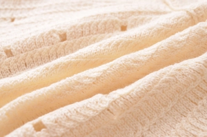 Close-up of cream knit dress fabric featuring cable stitch and hollow-out patterns